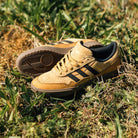 A pair of JI0851 Mesa Black Gum Tyshawn 2 II Adidas Leather Suede Skateboarding Shoes, tan with black stripes, rest on grass in sunlight, highlighting their cupsole construction from both side and top views.