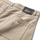 Close-up of JM5832 Gray Clay Kader Sylla Pant by Adidas, showing white Trefoil logo embroidery and a black Adidas x Kevin signature patch above the pocket; classic straight-leg skateboarding fit.