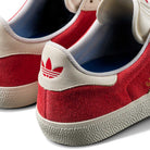 Close-up of the back of two JP5861 Red White Gold Gazelle ADV Adidas Skateboarding suede shoes with white leather heel tabs, red Trefoil logos, and textured white rubber soles.