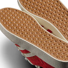 Close-up of the soles of two JP5861 Red White Gold Gazelle ADV Adidas Skateboarding Suede Shoes, featuring a honeycomb hexagonal tread and textured gray sides, positioned side by side to display the outsoles and part of the uppers.