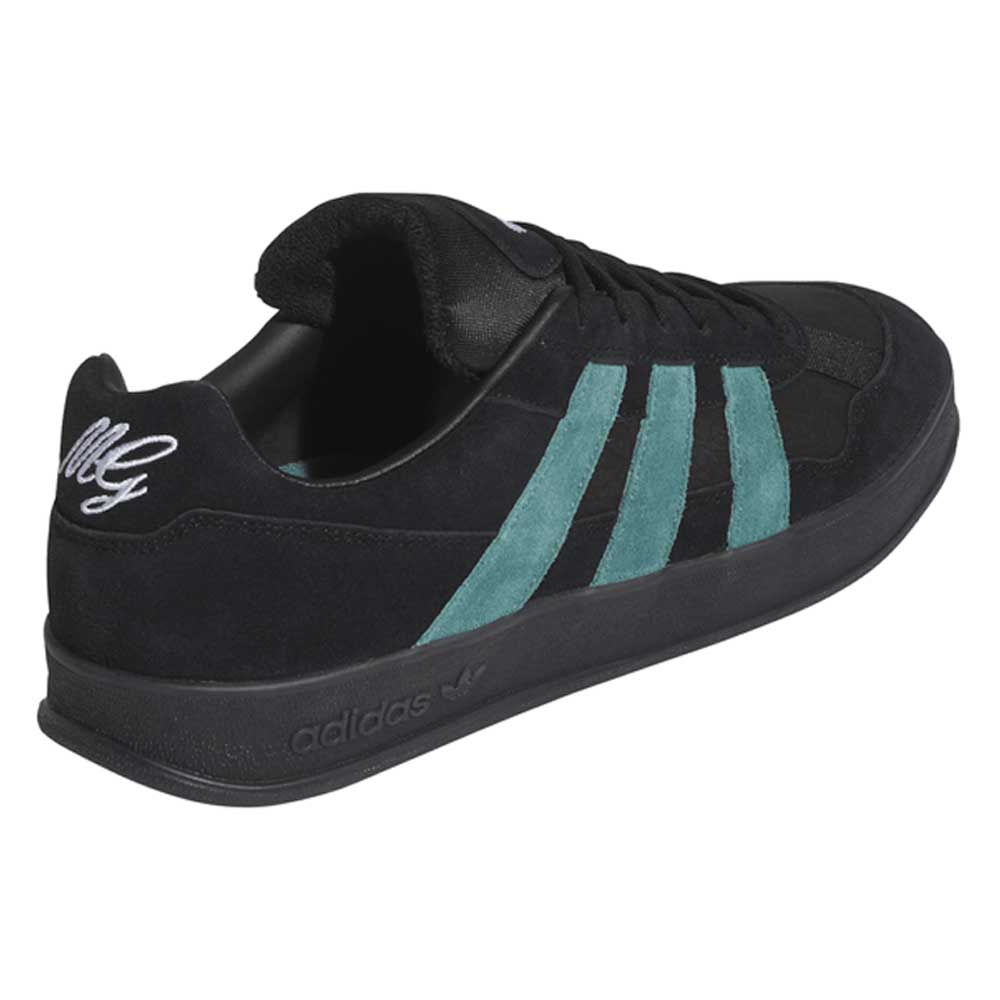 The JQ1042 Black Prete Aloha Super Suede Leather Skateboarding Shoes feature black suede, teal stripes, a black sole, and white “MG” heel embroidery. The low-top design and padded collar provide comfort and board control for skaters.