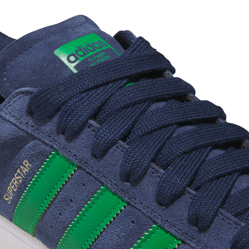 Close-up of JQ2098 Navy Green White Superstar ADV Adidas suede skateboarding shoes featuring a green Adidas tongue label, green stripes, yellow "SUPERSTAR" text, dark blue laces, and durable cupsole construction.