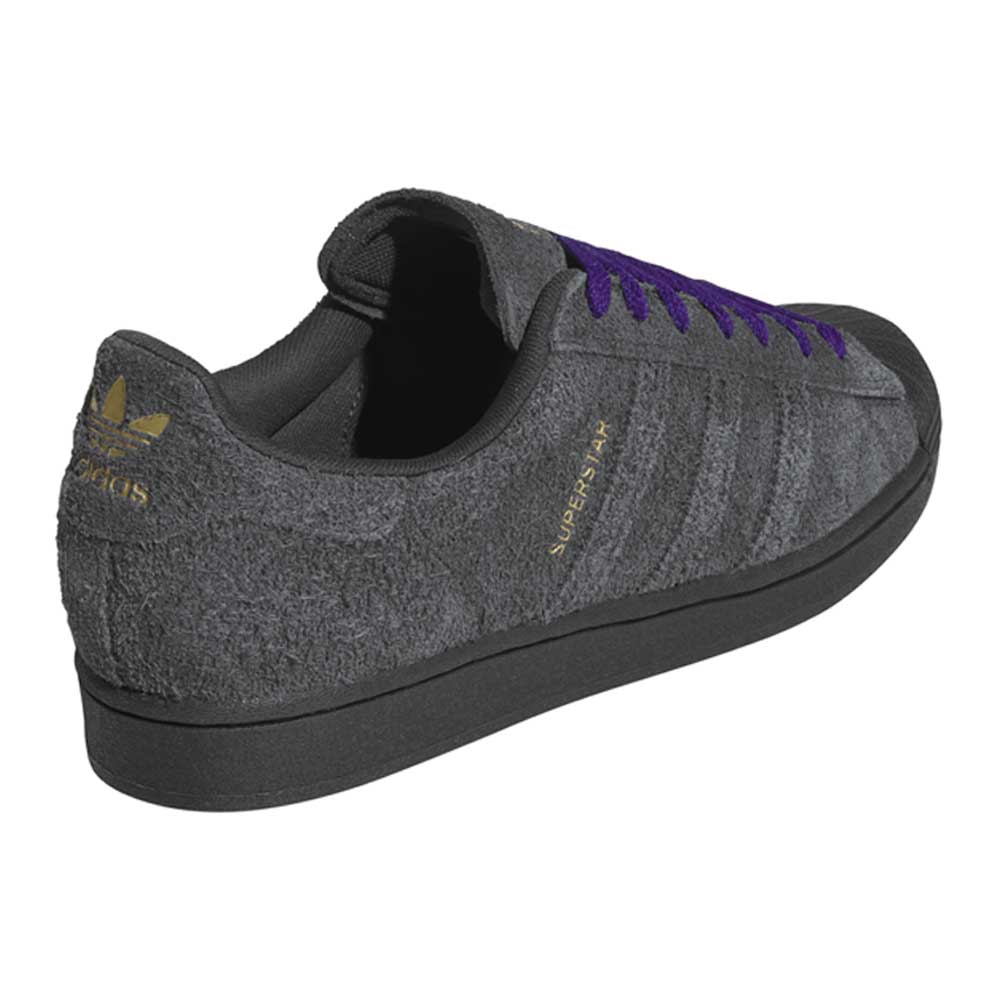 The JR7409 Carbon Purple Superstar ADV Adidas suede skateboarding shoe features a dark gray and purple suede upper, black sole, gold Adidas logo and “Superstar” text, plus purple laces—shown from the back left side.