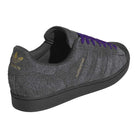 The JR7409 Carbon Purple Superstar ADV Adidas suede skateboarding shoe features a dark gray and purple suede upper, black sole, gold Adidas logo and “Superstar” text, plus purple laces—shown from the back left side.