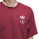 Someone wearing the JW0056 Skate Tee Burgundy Adidas Skateboarding, which has three stacked white Adidas Trefoil logos on the left chest. The image is cropped to display only the upper torso and neck.