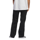 A person stands against a white background in a white T-shirt and the loose-fitting JX6827 Black Kader Sylla Pant by Adidas, shown from the back to highlight its cotton twill fabric. Only the lower body is visible in the cropped image.