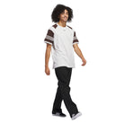 A young man with curly hair walks confidently in a white T-shirt with brown short sleeves with white stripes, JX6827 Black Kader Sylla Pant Adidas made from cotton twill, and black sneakers with white stripes, against a plain white background.