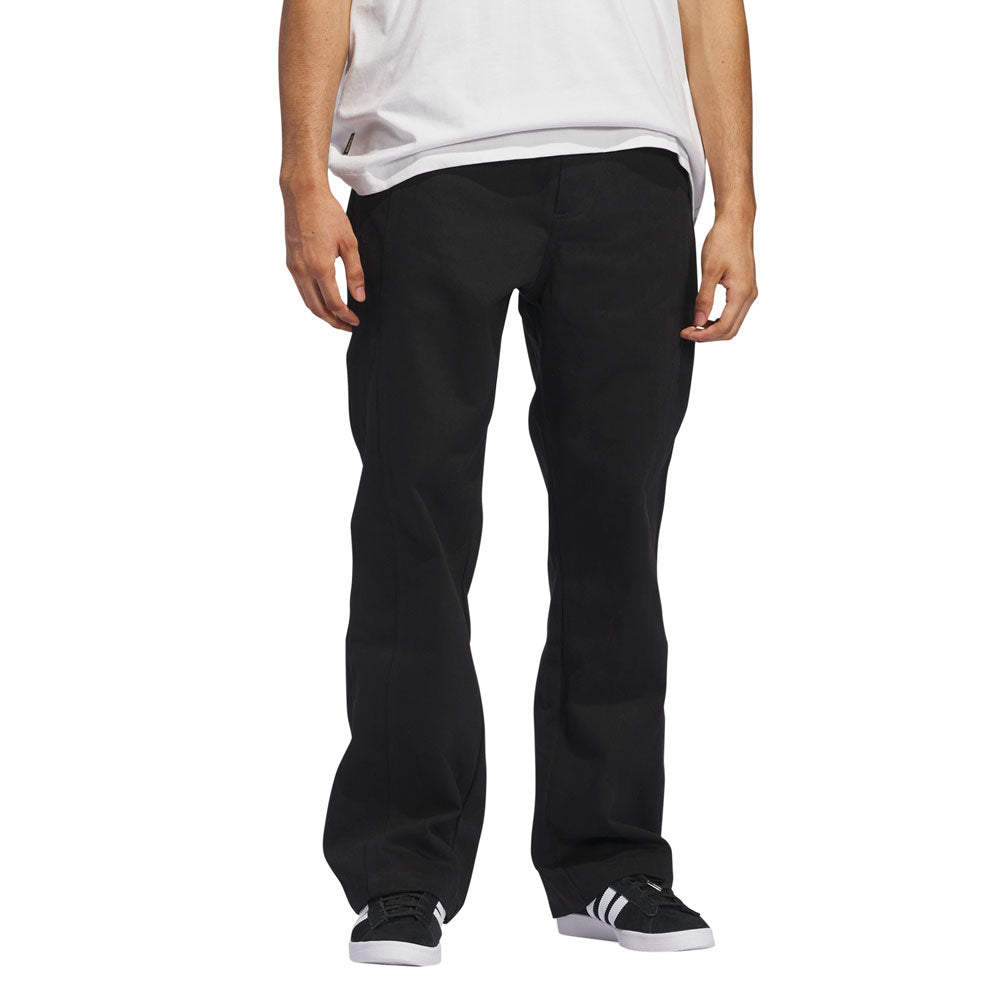 A person is standing against a white background, shown from shoulders down, wearing a white T-shirt, JX6827 Black Kader Sylla Pant Adidas, and black-and-white sneakers.