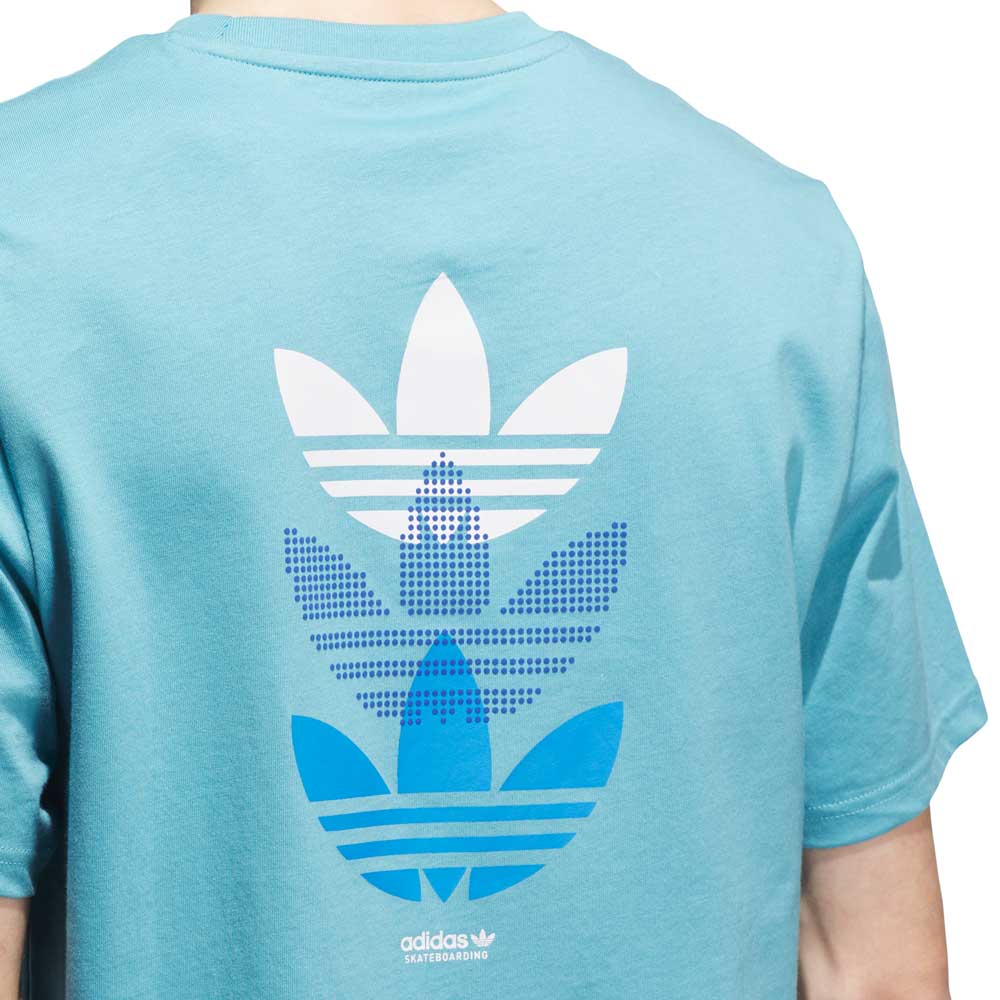 A person wearing the JY3954 Skate Tee in Preloved Blue/Bright Royal, featuring three stacked blue and white Adidas trefoil logos and "Adidas Skateboarding" text on the back.