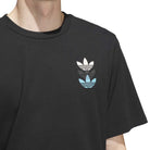 A person wears the black JY3955 Skate Tee from Adidas Skateboarding, featuring three stacked Trefoil logos (white, black, blue) on the chest. Only their upper body is shown. Imported product.