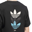 A person wearing a black JY3955 Skate Tee by Adidas Skateboarding, an imported product, with three vertically stacked trefoil logos in cream, white with dots, and blue on the upper back.