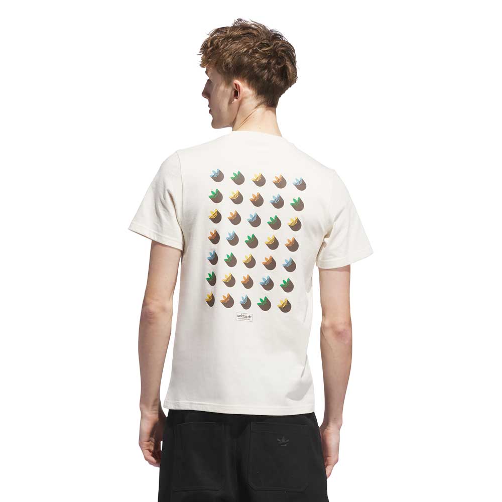 A person with short, light brown hair is seen from behind wearing the JY3958 Skate Tee in Wonder White/Rustic Orange by Adidas Skateboarding, featuring colorful trefoil logos on the back, paired with black shorts.