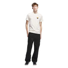 A young man with short, curly hair wears the JY3958 Skate Tee in Wonder White Rustic Orange from Adidas Skateboarding, paired with black pants and sneakers, standing against a plain white background.