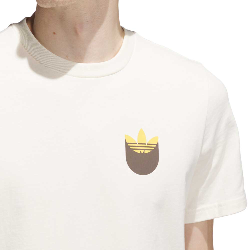 A person wearing the JY3958 Skate Tee in Wonder White with a rustic orange Adidas trefoil logo on the chest. Imported product from Adidas Skateboarding.