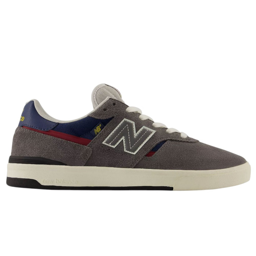 A side view of the Jamie Foy Cup 306 CON New Balance Numeric Suede Skateboarding Shoes in gray, featuring white laces, blue and red accents, a white midsole, black rubber cup outsole, and the iconic N logo—these durable suede skate shoes are designed for ultimate performance and style inspired by Jamie Foy.