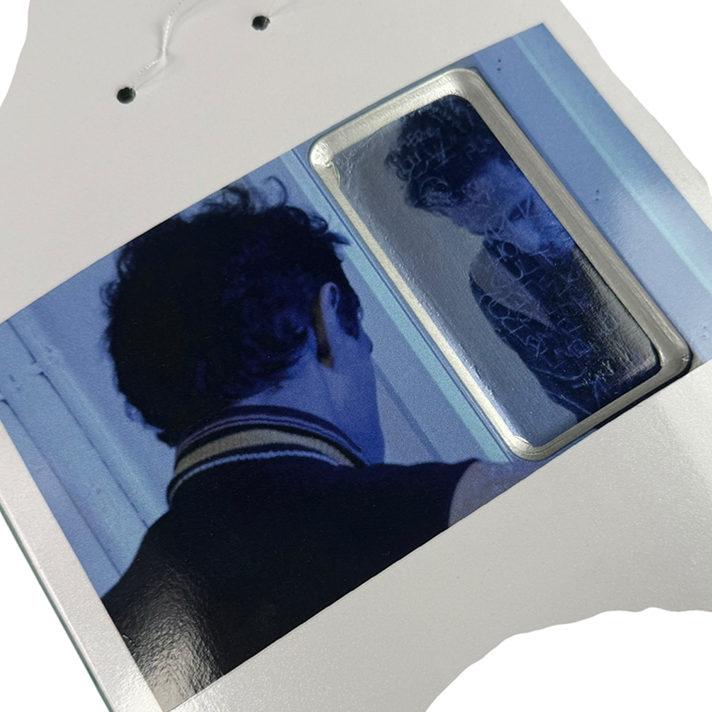 A person with short dark hair and a striped collar is seen from behind, looking into a mirror. Reflected next to them is the Jim Greco Hammers 3 Board Deck Set Collectible, in an image with a cool blue tint.