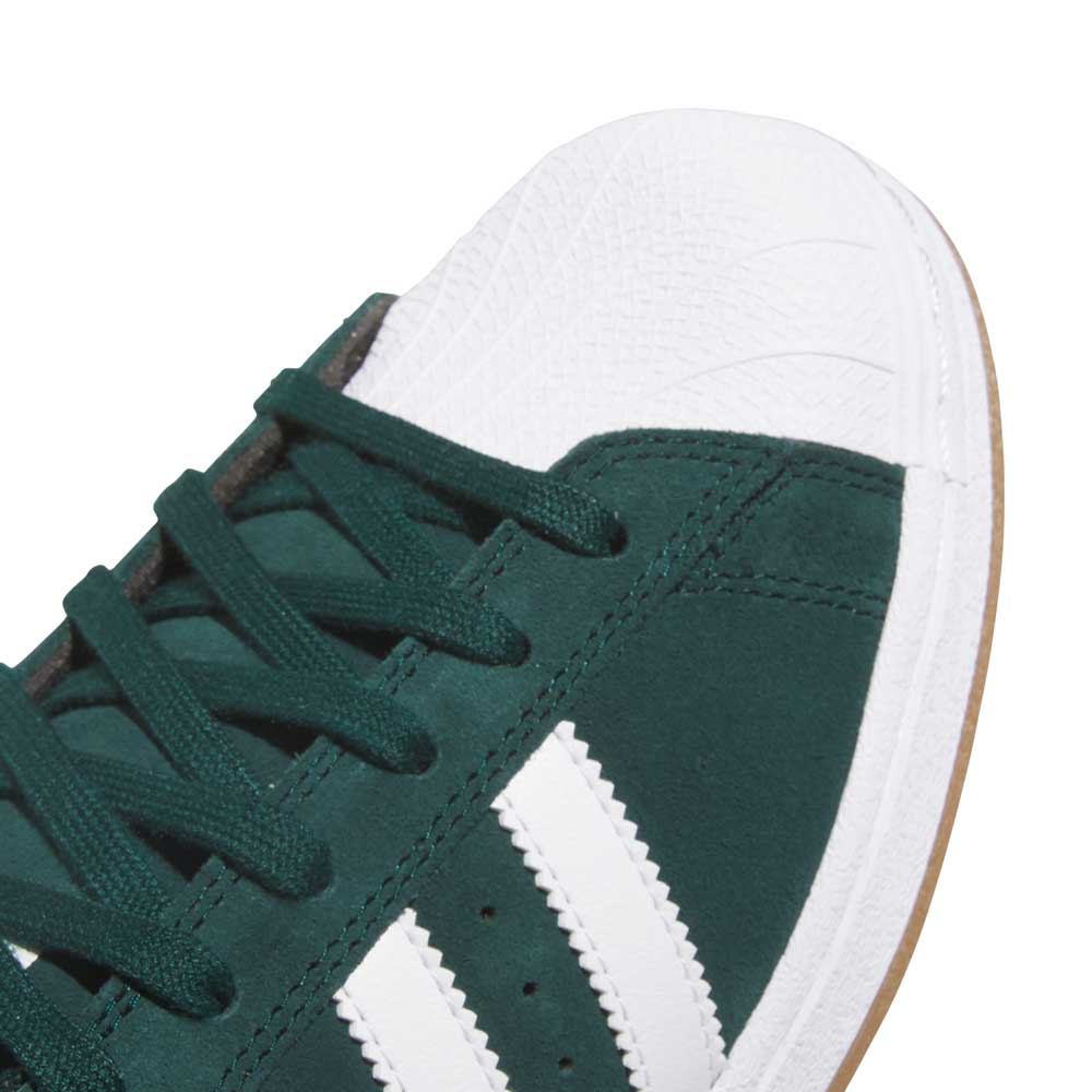 Close-up of the KI5732 Green White Superstar ADV Adidas Skateboarding Suede Shoes, showing white stripes, a white textured toe cap, dark green laces, and a gum-colored sole—perfect for skateboarding. Photographed on a white background.