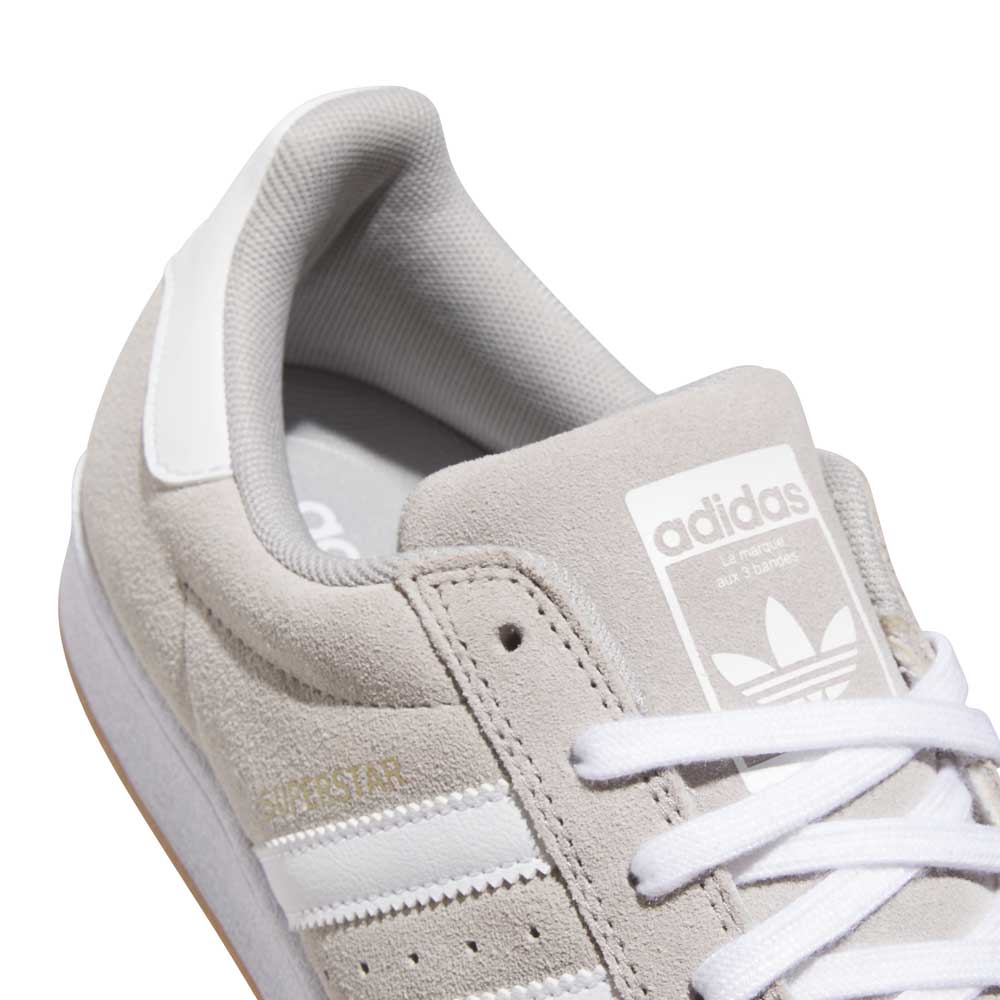Close-up of the KI5733 Gray White Superstar ADV Adidas Skateboarding Suede Shoes, featuring a light grey suede upper, white stripes, heel tab, and laces. This classic low-top design showcases the Trefoil on the tongue—ideal for stylish skateboarding.