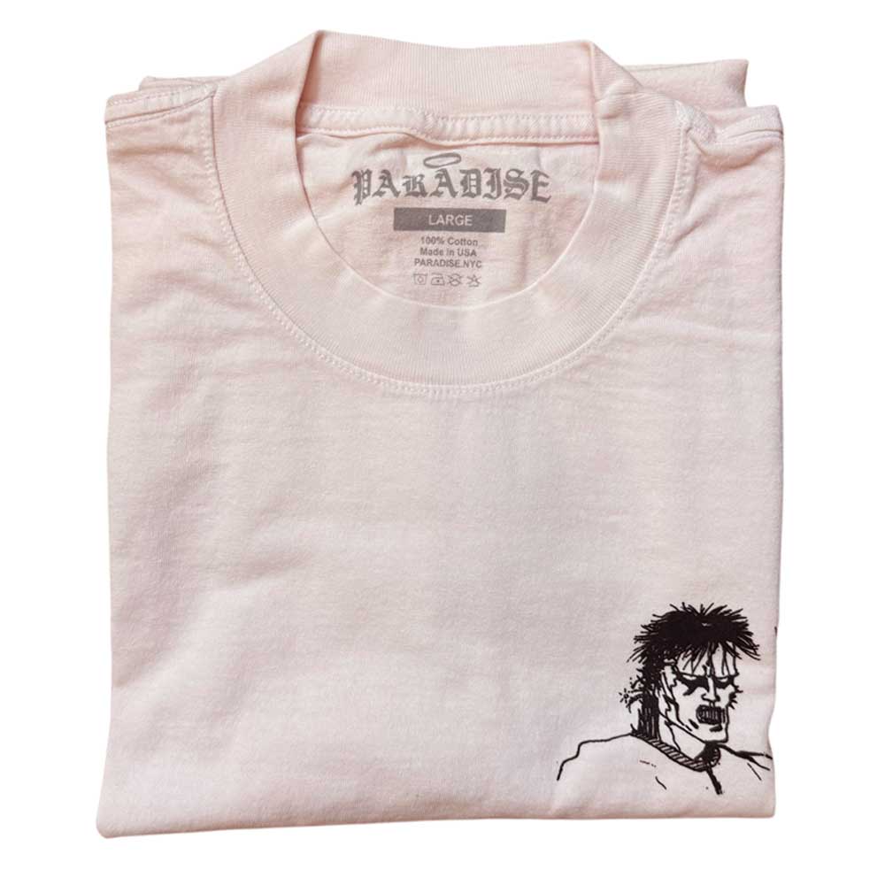 The Kill Kill Kill Light Pink Tee Paradise is a folded, pale pink garment-dyed t-shirt made from soft USA cotton. It features a small black spiky-haired anime face near the hem and “PARADISE” printed inside the collar.