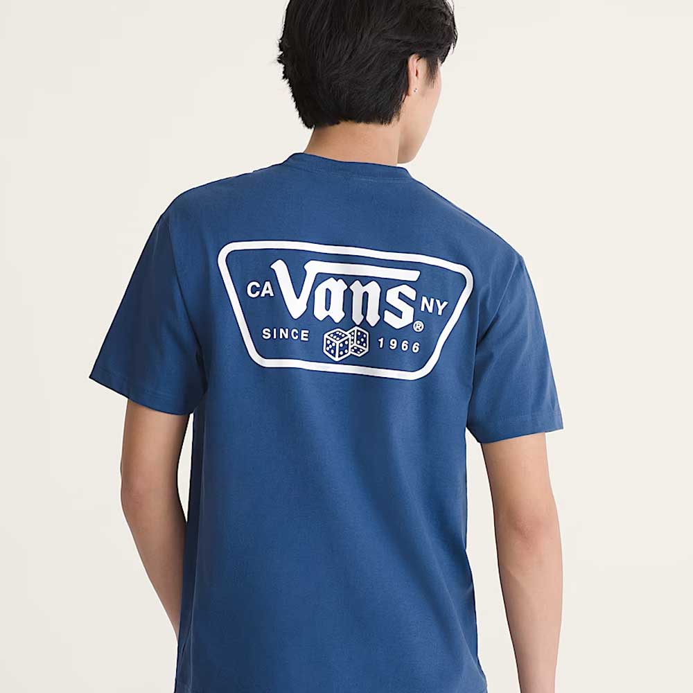 A person wears the Knu Patch VN000WU85TU1 True Navy Blue Short Sleeve Tee from Vans Skateboarding, a loose-fit 100% cotton shirt with a large white Vans logo and dice graphic, plus "CA NY, Since 1966" on the back, against a plain background.