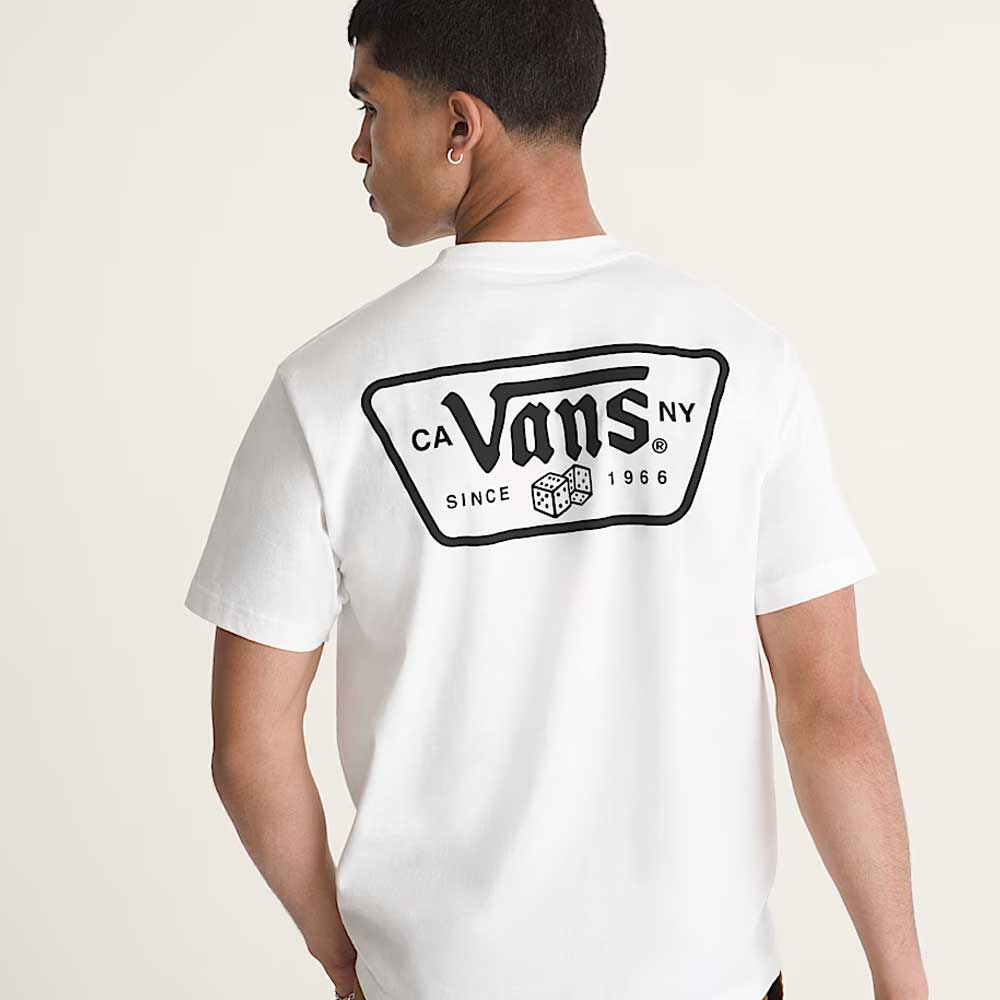 A person seen from behind wears a loose-fit Knu Patch VN000WU8WHT1 White Short Sleeve Tee by Vans Skateboarding, made of 100% cotton, with a large black Vans logo and text on the back, standing against a plain light background.