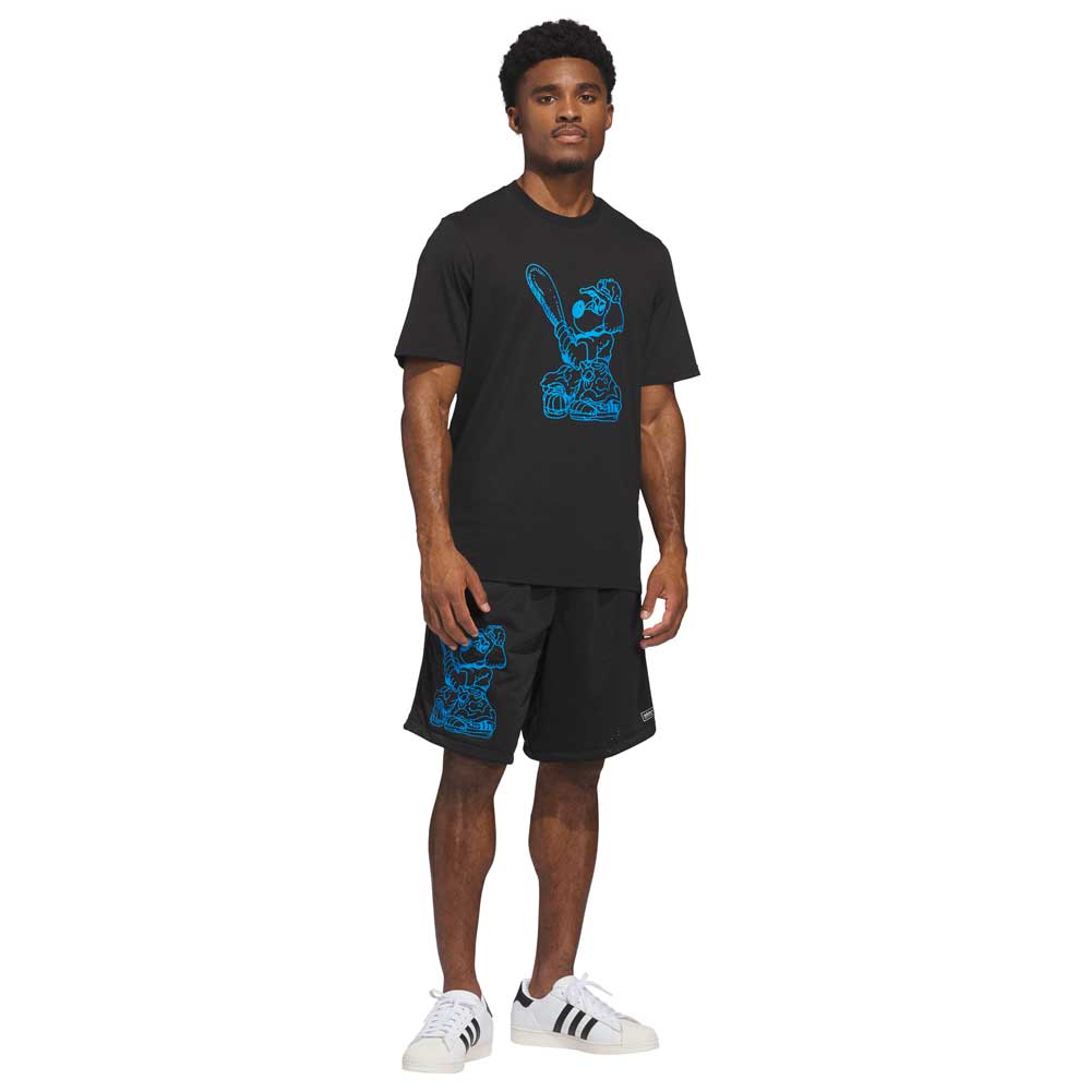 A man stands facing forward, wearing the Kogan Dog Tee Black Blue KC6304 Adidas Skateboarding and black shorts with blue bear graphics, paired with white Adidas sneakers with black stripes.
