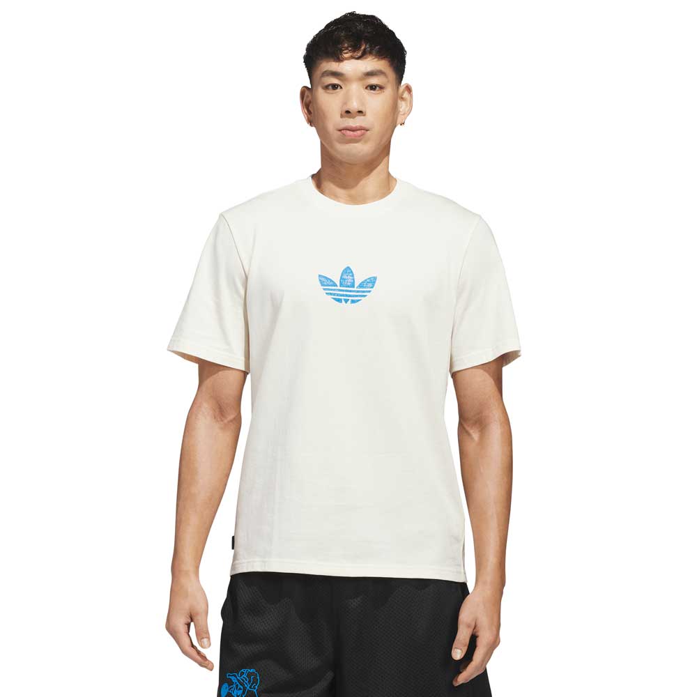A person faces forward wearing the Kogan Dragon Tee Cream Blue KC6305 from Adidas Skateboarding with a blue trefoil logo, paired with black shorts, against a plain white background.