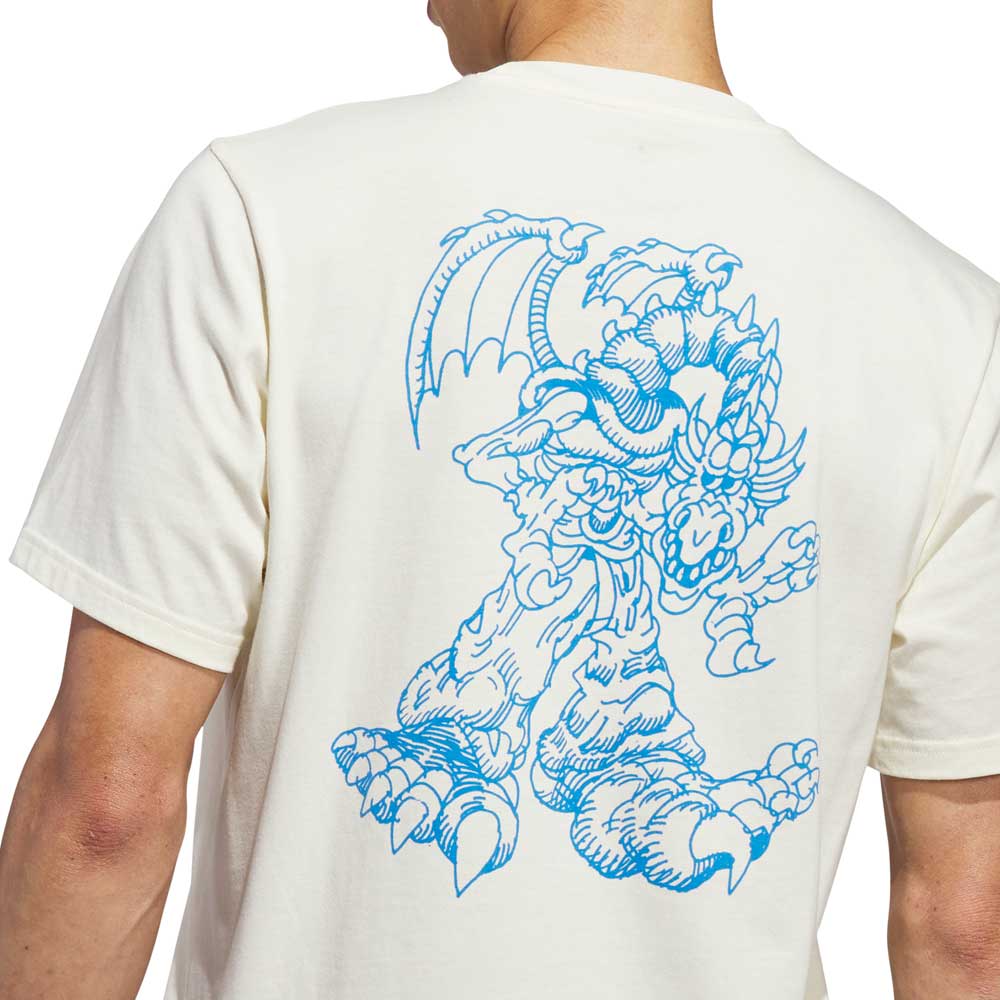 A person is seen from behind wearing the Kogan Dragon Tee Cream Blue KC6305 by Adidas Skateboarding, featuring a large blue line drawing of a winged dragon on the back—a nod to skate culture style.