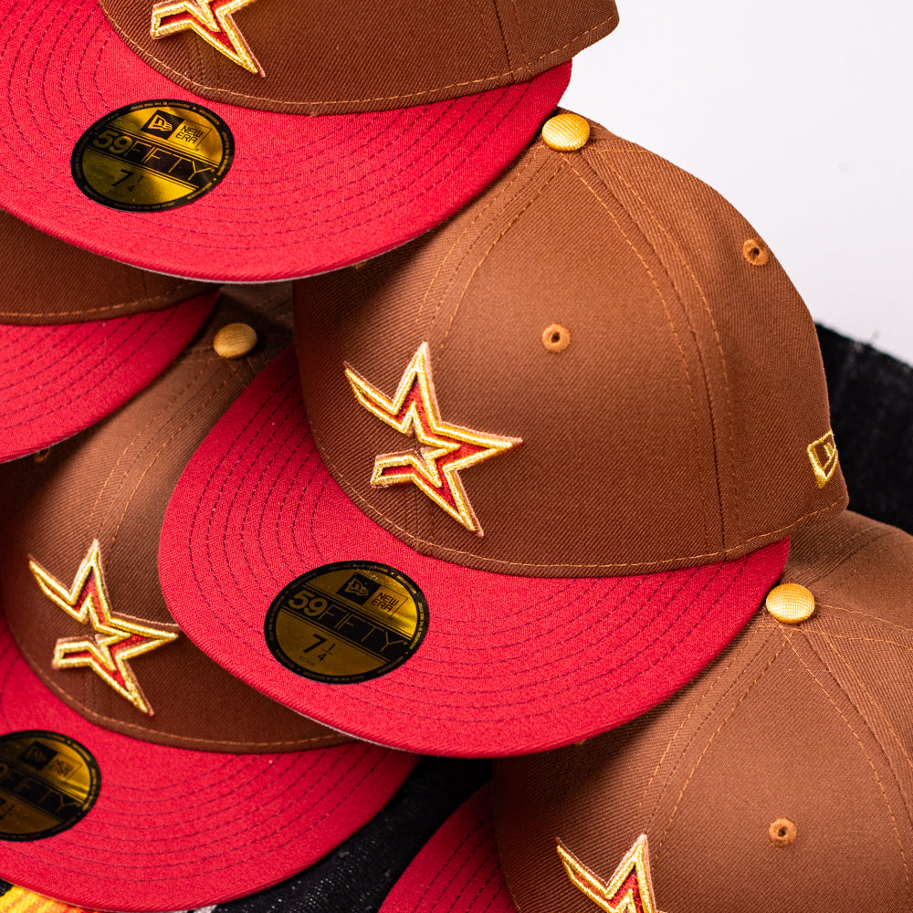 A stack of Bendicion de la Abuela 20th Brown Red Houston Astros New Era Hat 5950 Fitted hats, featuring a yellow star logo and gold size 7 stickers, neatly arranged in an overlapping pattern.