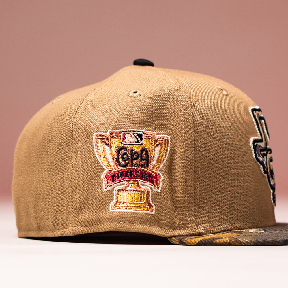 The La Ofrenda Khaki RTC Copa Corpus Christi Hooks New Era 5950 Fitted hat features an embroidered golden trophy patch reading Copa Diversión with the MLB logo above, a camouflage brim, and a soft pink gradient background.