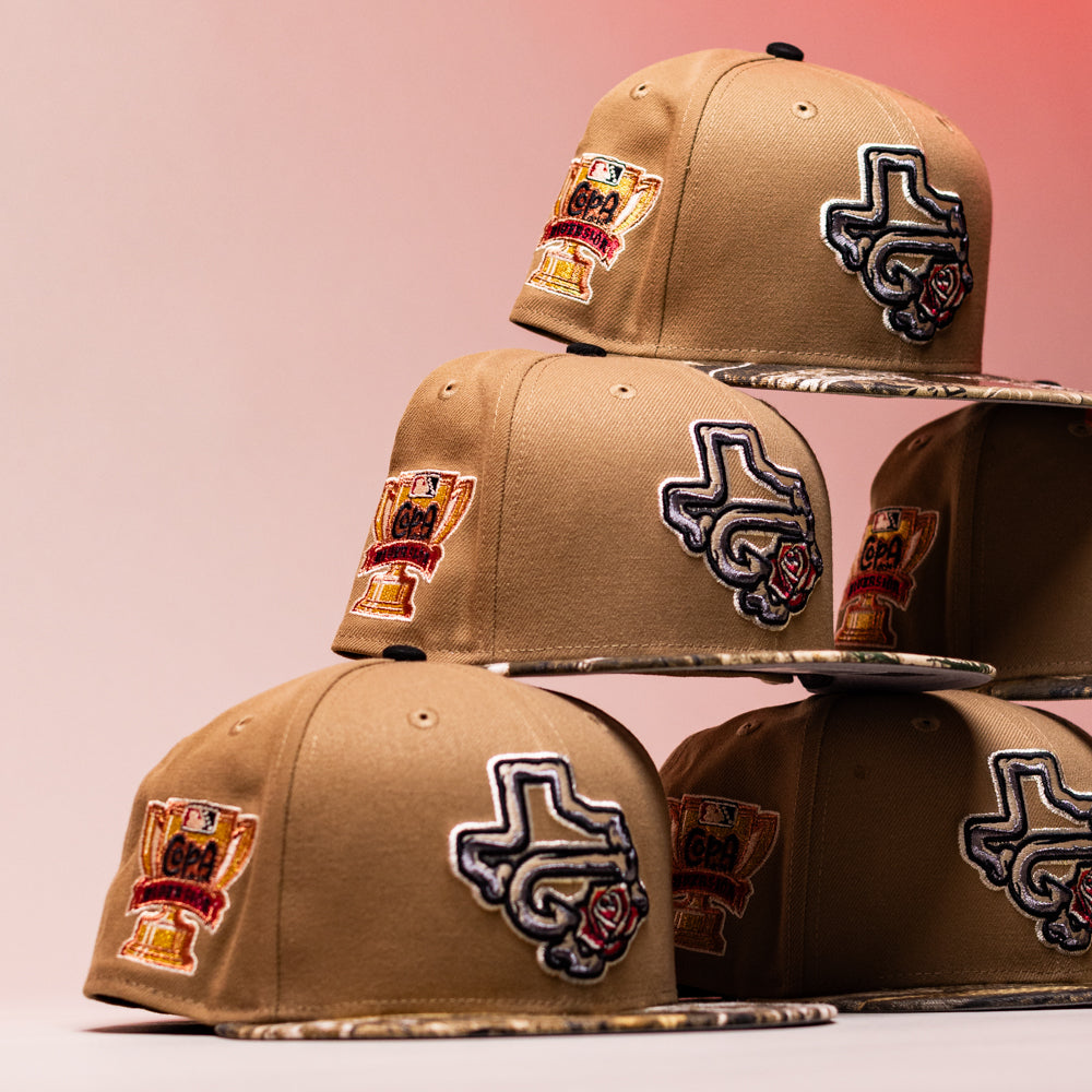 Five La Ofrenda Khaki RTC Copa Corpus Christi Hooks New Era 5950 fitted hats are stacked in two tiers. Each features multicolored embroidered Texas and trophy patches, set against a pink gradient background.