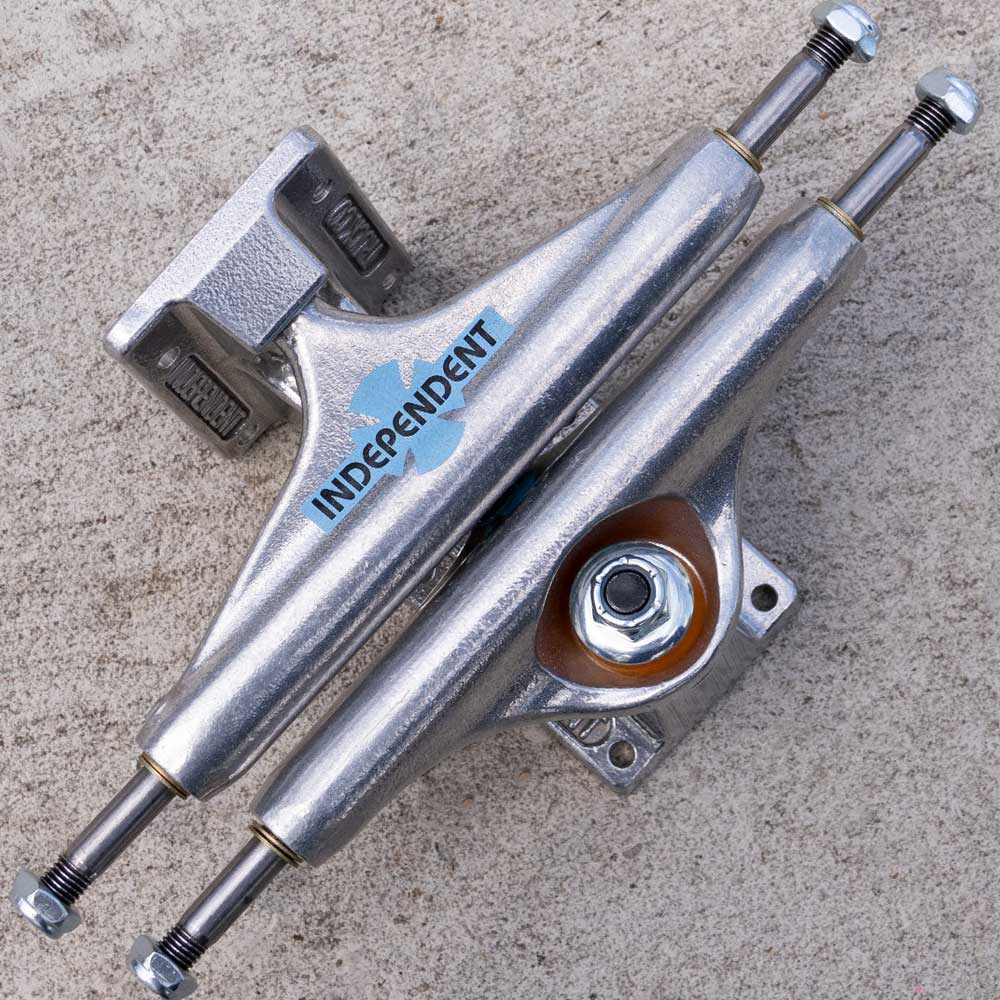 Two Legacy OGBC INDY 139 Polished Silver Standard Stage 11 skateboard trucks are stacked in an X shape on a rough, light-colored concrete surface. The kingpin and bushings are visible on the lower truck, highlighting the durable aluminum construction of these standard Stage 11 trucks built to handle every ride.