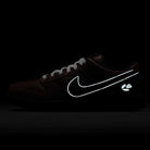 The HJ4131-200 Limosine Dark Pony Black Silver White Nike SB Dunk Low Pro skateboarding shoe features a black upper, glowing white swoosh, and reflective paw print on the heel, displayed against a dark background.