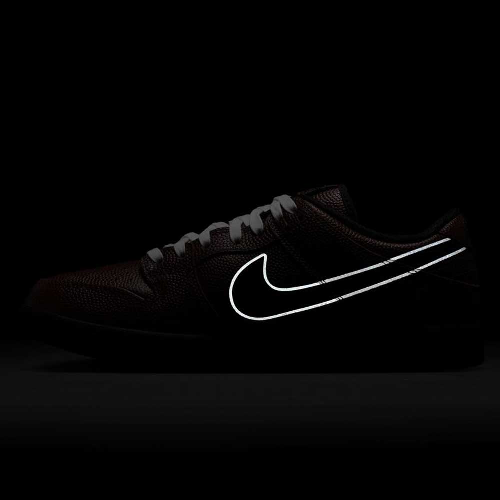 The HJ4131-200 Limosine Dark Pony Black Silver White Nike SB Dunk Low Pro Skateboarding Shoe is displayed in low light, with its white Swoosh logo glowing boldly against the dark backdrop.