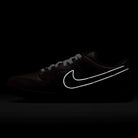 The HJ4131-200 Limosine Dark Pony Black Silver White Nike SB Dunk Low Pro Skateboarding Shoe is displayed in low light, with its white Swoosh logo glowing boldly against the dark backdrop.