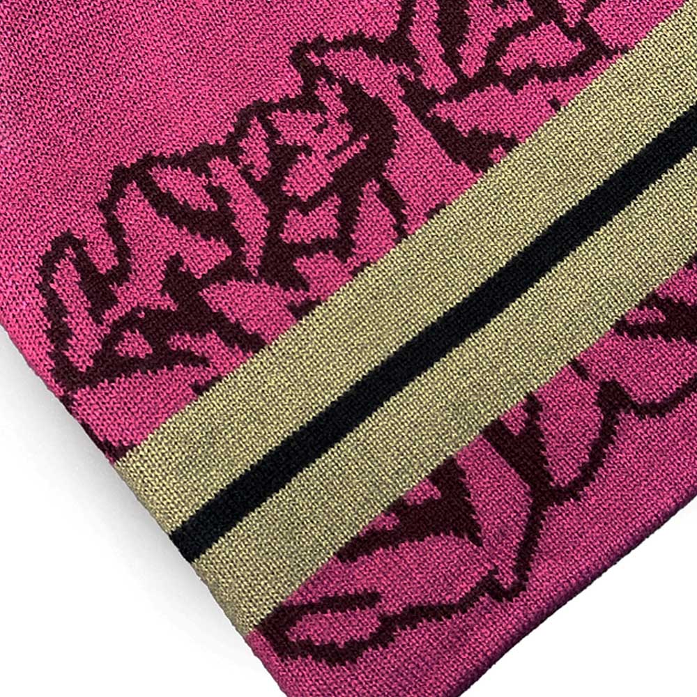 Close-up of the Striped Beanie Red Late Nite Stars Skateboarding, showing its pink knit fabric with a black floral pattern and two diagonal gold and black stripes.