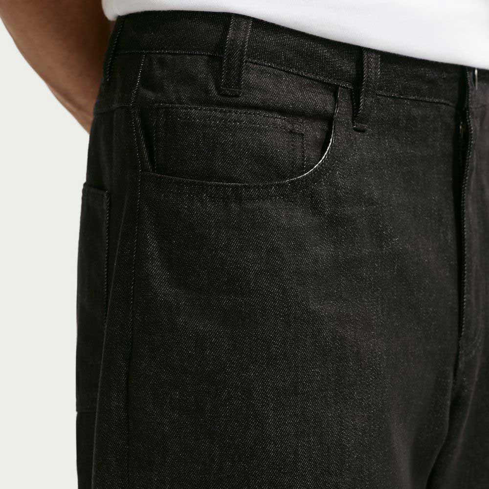 Close-up of a person wearing Loose Denim Black Pant IB2992010 Nike SB, featuring a jacron label, white shirt, upper waist, front pocket, and belt loops. Made from 100% cotton for comfort and durability.