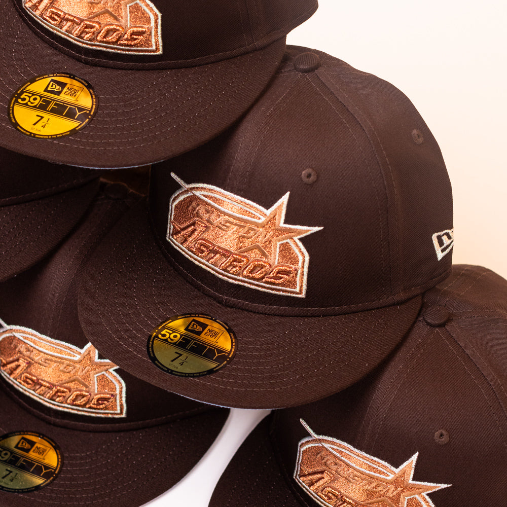 A stack of black Muddy Waters Houston Astros New Era 5950 Fitted hats with copper logos and gold sizing stickers, viewed from above, showcases the iconic style of this premium fitted cap.