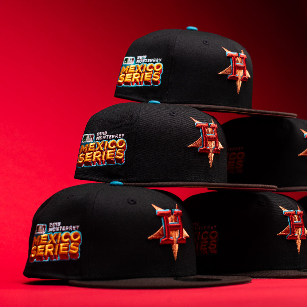 Four black-and-brown Prisa Cero 2.0 Houston Astros New Era 5950 fitted hats, each featuring the 2019 Monterrey Mexico Series and a red-orange Astros H logo, are stacked in two rows against a vibrant red background for a bold style statement.