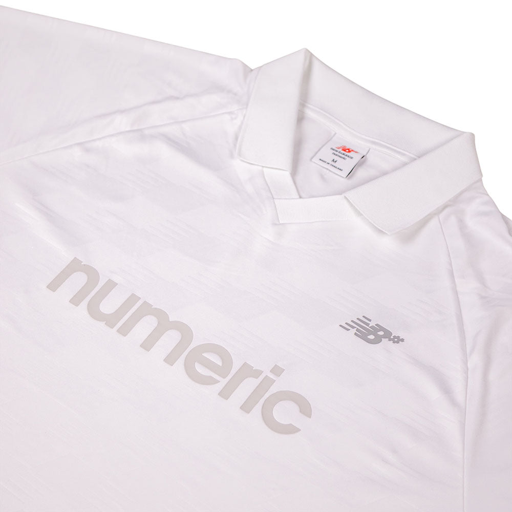 A close-up of the New Balance Numeric Team Jersey MT61V471ABR, a white collared shirt with ‘numeric’ and the New Balance logo in light gray on the front, subtle textured patterns, and a visible inner collar label.