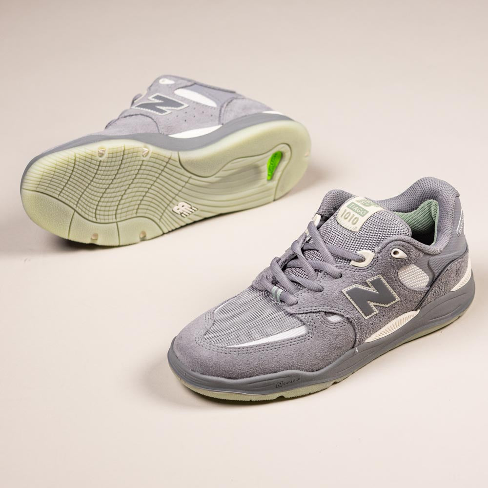 A pair of 1010 PS Tiago Lemos Slate Grey Sea Salt New Balance Numeric suede skateboarding shoes, one on its side displaying the sole and the other upright, are placed on a light-colored surface.