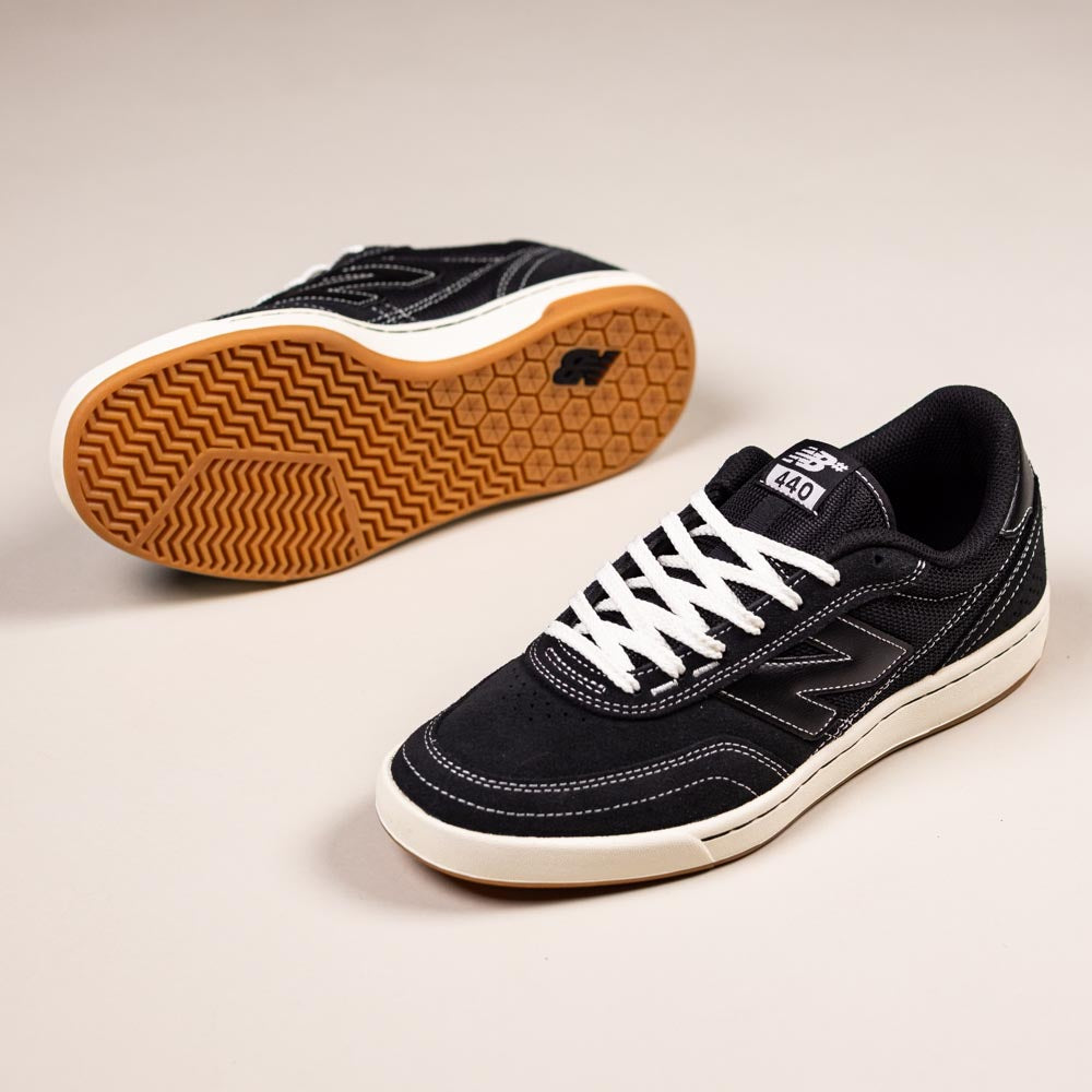 A pair of 440 BCO Black White New Balance Numeric Suede Skateboarding Shoes: one shoe stands upright showing the side and top, while the other is on its side revealing the brown tread and durable ABZORB midsole.