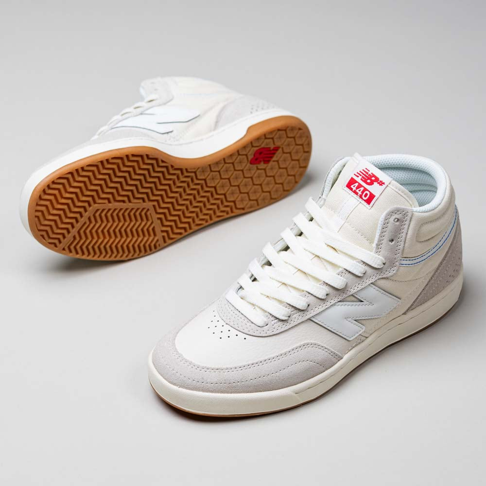 A pair of Timberwolf White New Balance Numeric 440 HTW skateboarding shoes with light gray suede accents, gum rubber soles, and red tongue branding. One shoe stands upright while the other shows its textured sole.