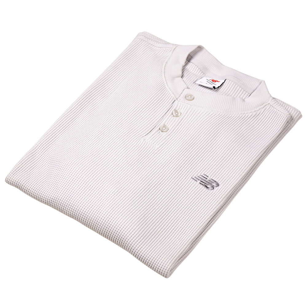 The New Balance Numeric Waffle Knit Tee MT51958GYM is a folded, light gray thermal with long sleeves, three buttons, and the New Balance logo embroidered on the chest.