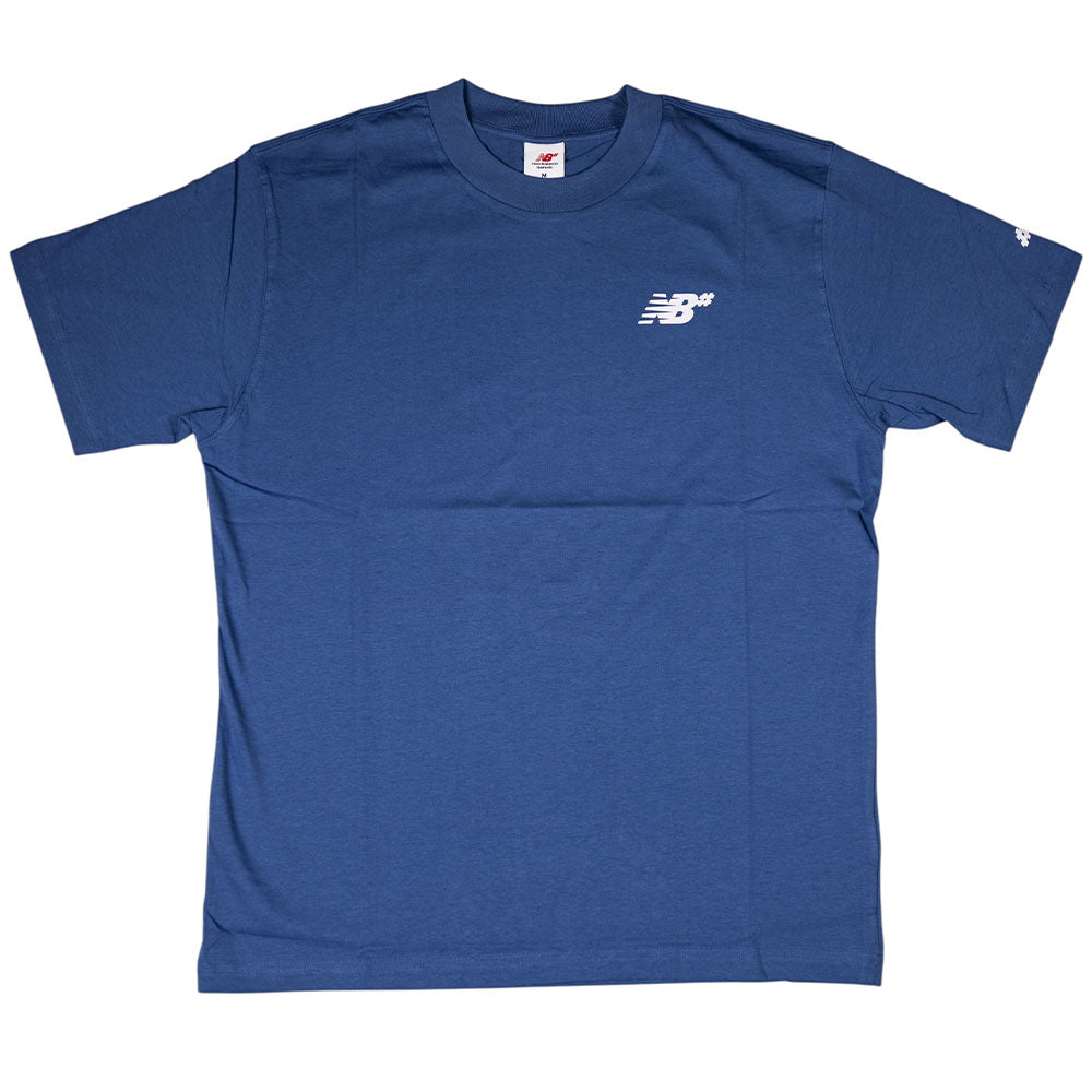 The New Balance Numeric Small Logo Magic Blue Tee MT53706AA4 is a relaxed fit cotton crewneck in plain blue with a small white logo on the chest and a white symbol on the left sleeve, shown laid flat on a white background.