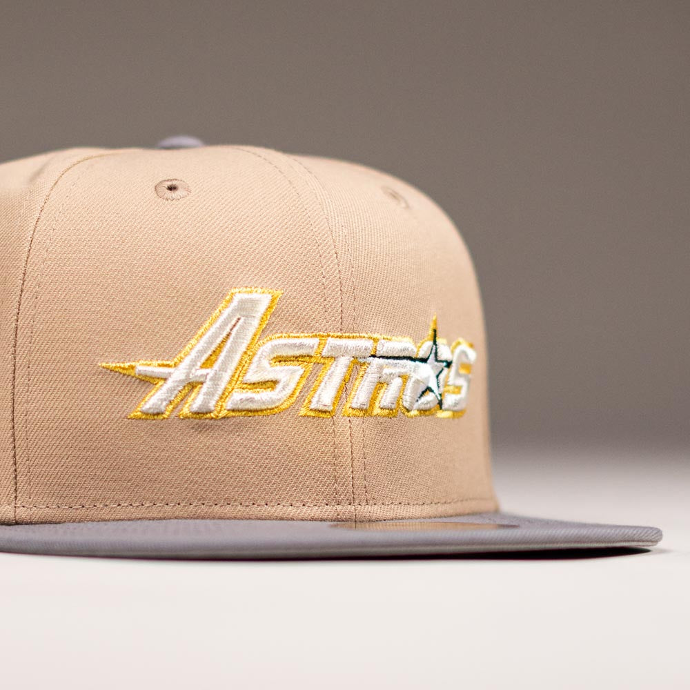 The Chalino Skull Camel Storm Houston Astros New Era 59FIFTY fitted hat features a beige crown, gray brim, and "Astros" embroidered in yellow, white, and gray on the front. The background is plain and out of focus.