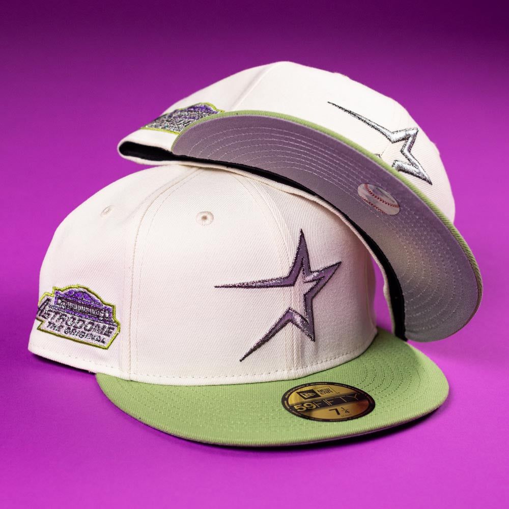 Two Matcha Guy Houston Astros New Era 5950 Fitted Hats in white and light green, featuring a star logo front and side patch, are displayed on a purple background—one flat, one propped to show the underbrim.