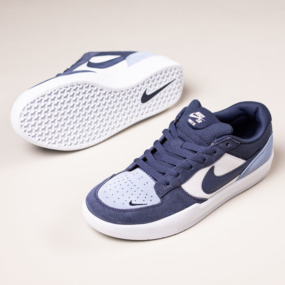 A pair of Nike SB Force 58 Suede Skateboarding Shoes in Light Armory Blue/Thunder Photon Dust (DV5477-404), with one shoe upright and the other on its side showing the textured sole, Swoosh logo, and heritage basketball design.