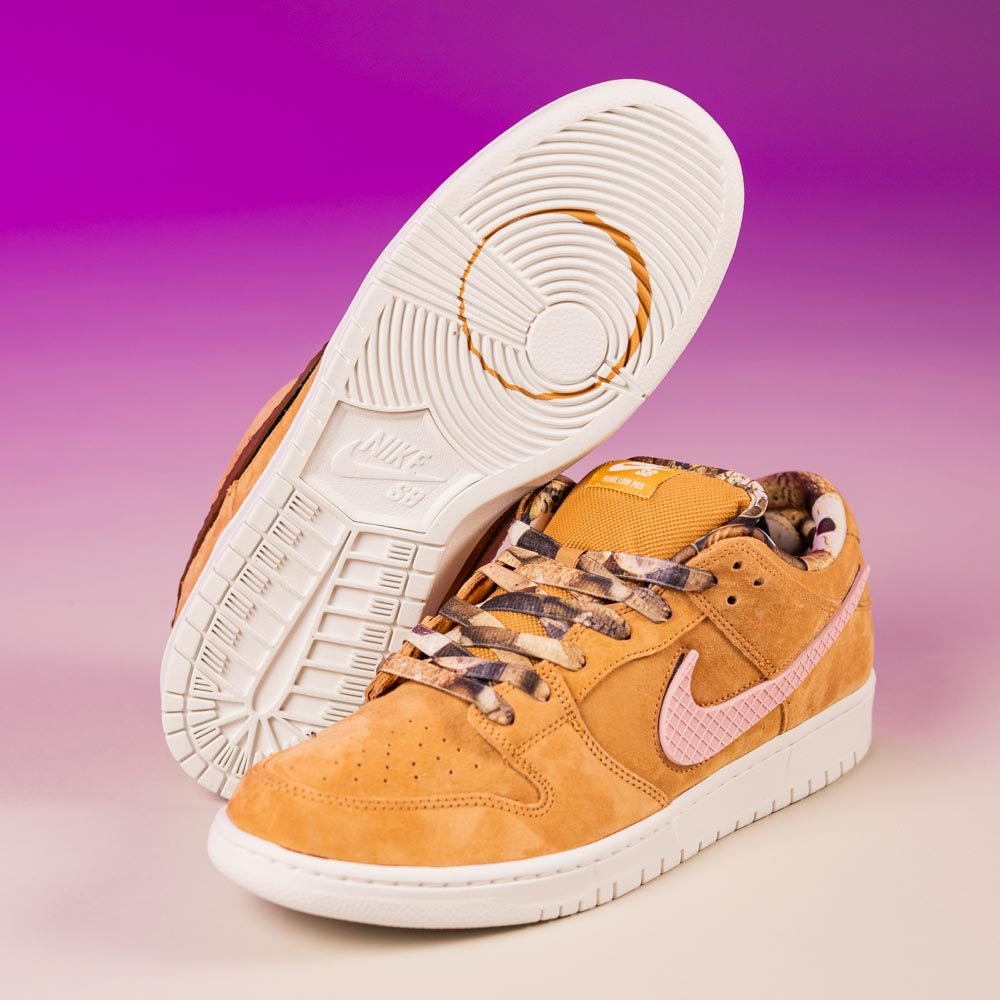 A pair of tan READ BELOW the BUTTON RAFFLE Nike SB Brew and Biscuits Dunk Low sneakers with pink swooshes and white soles, set against a purple-beige gradient—perfect for your next Southside Skatepark raffle entry.