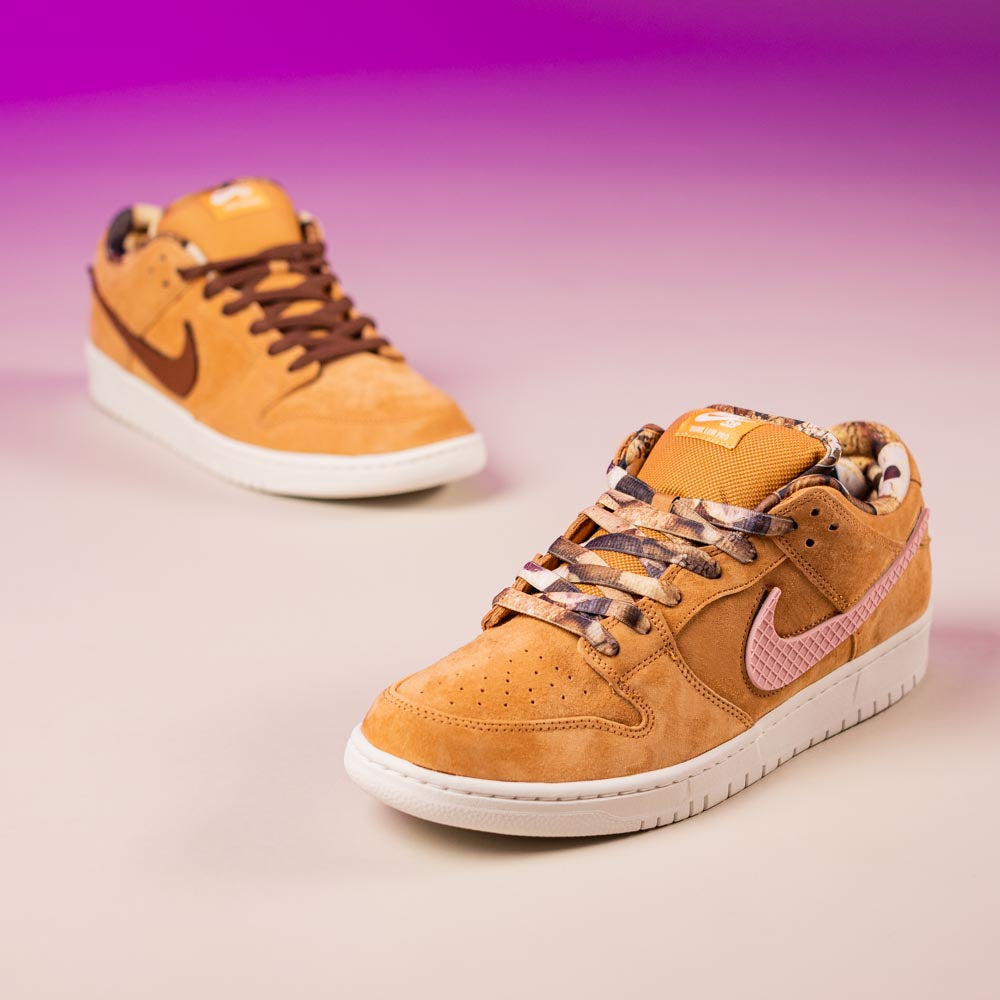 A pair of tan READ BELOW the BUTTON RAFFLE Nike SB Brew and Biscuits Dunk Low sneakers with patterned laces and pink swooshes are displayed on a beige surface with a purple gradient background—perfect for Southside Skatepark's raffle entry.